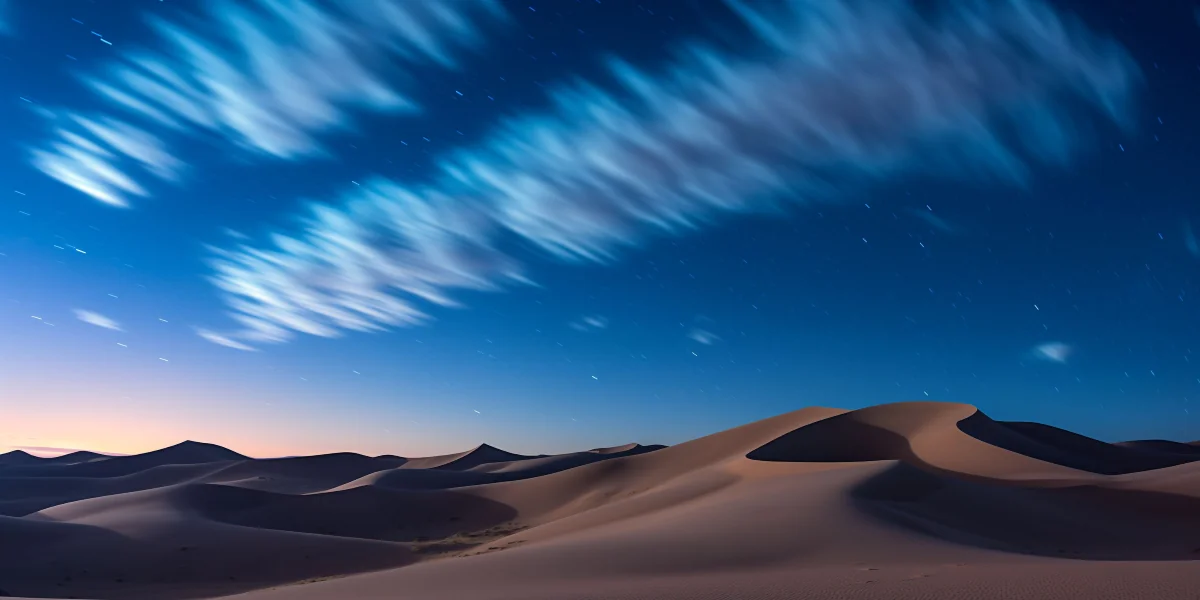 A star-filled night sky stretches over pale desert dunes.