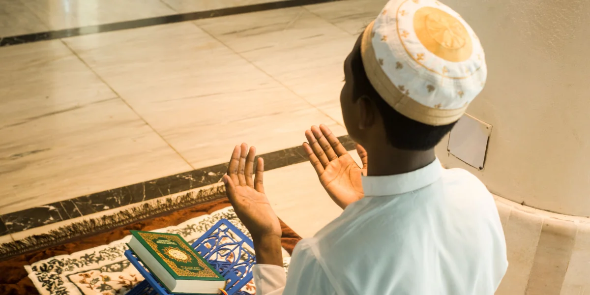 A young Muslim man praying indoors with the Quran in front of him, embodying devotion and peace.
