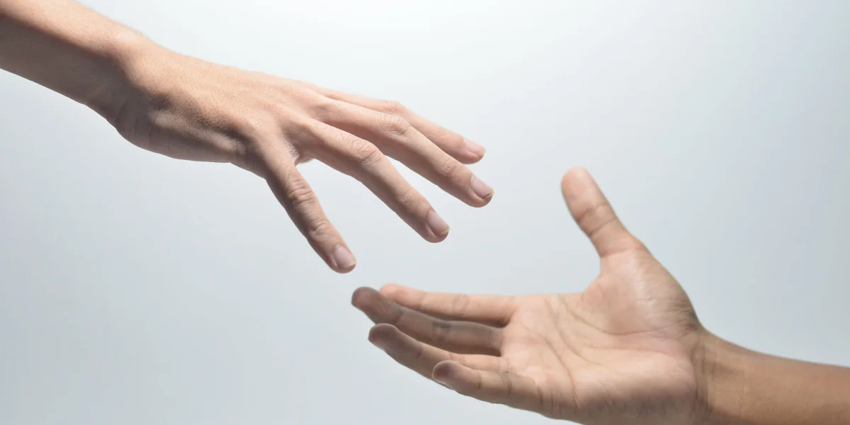 Close-up of two hands reaching towards each other on a neutral background, symbolizing help.